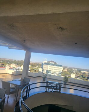 Un balcón con mobiliario de mimbre, una planta en maceta y vistas de edificios de la ciudad.
