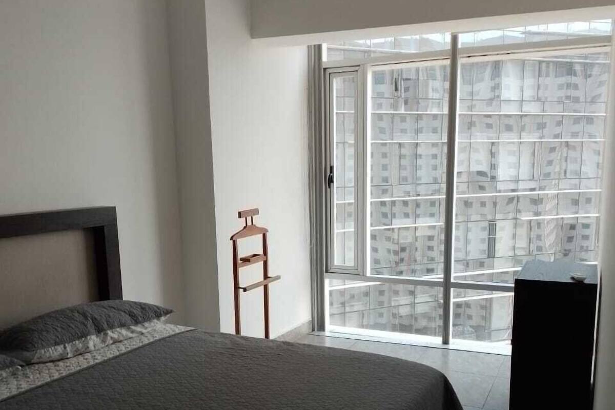 A bedroom with a large bed, a wooden hanger, and a view of a cityscape through a sliding glass door.