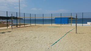 En strandvolleyballbane med net, sand og en blå bygning i baggrunden.