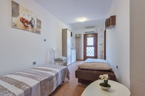 Een hotelkamer met twee bedden, een klein tafeltje met een bloem, een schilderij aan de muur en een deur met een raam.