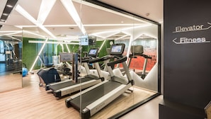 Ein moderner Fitnessraum mit Laufbändern, einem Rudergerät und einem an der Wand montierten Fernseher.