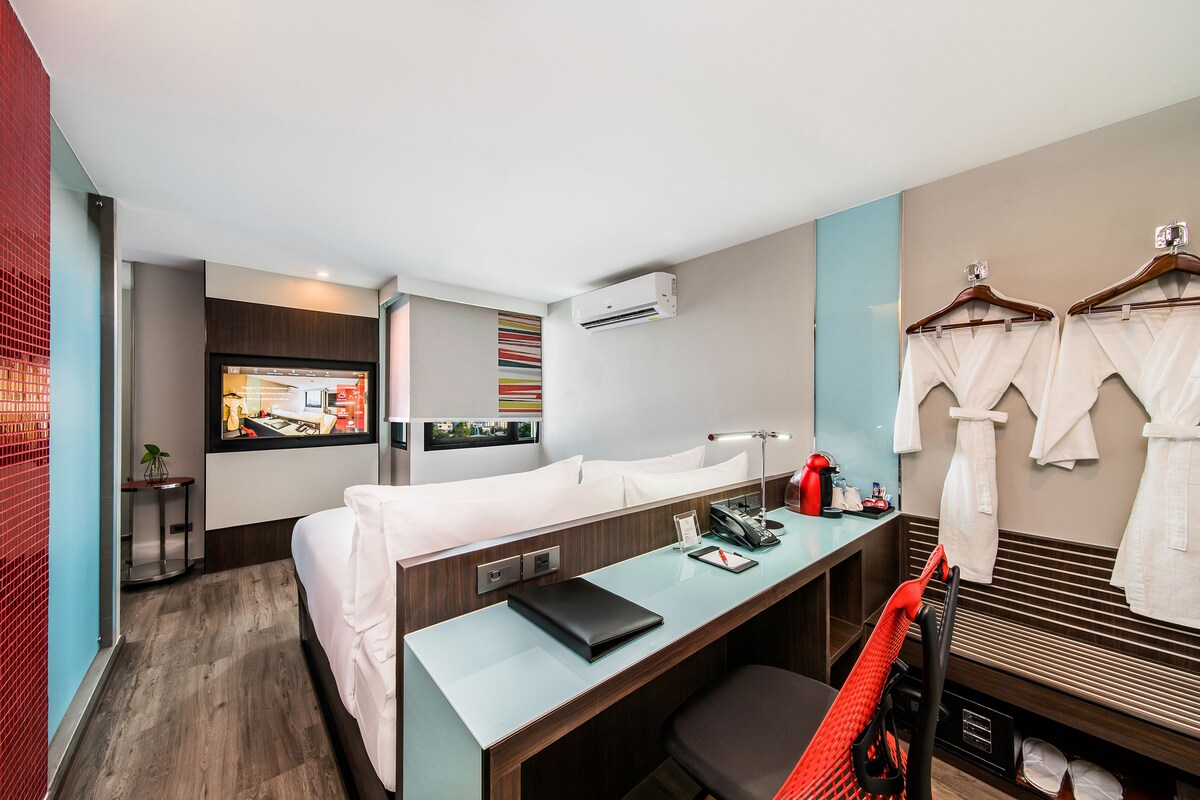 Een hotelkamer met een bed, bureau, stoel en een televisie waarop een plattegrond van de kamer wordt getoond.