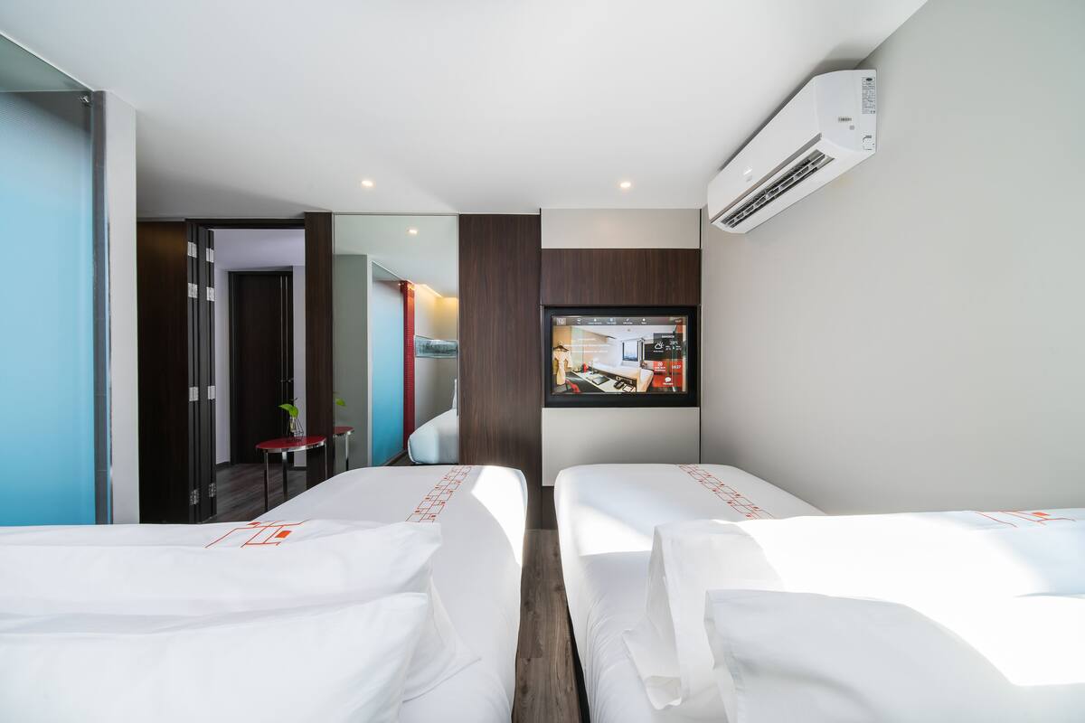 Une chambre d’hôtel avec deux lits, un téléviseur fixé au mur et un appareil de climatisation.