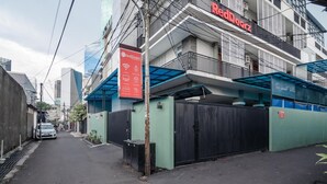 Una calle urbana estrecha con un área amurallada, un letrero de RedDoorz y edificios modernos al fondo.