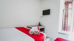 Una habitación de hotel con cama, escritorio, televisor y ventana con cortinas.