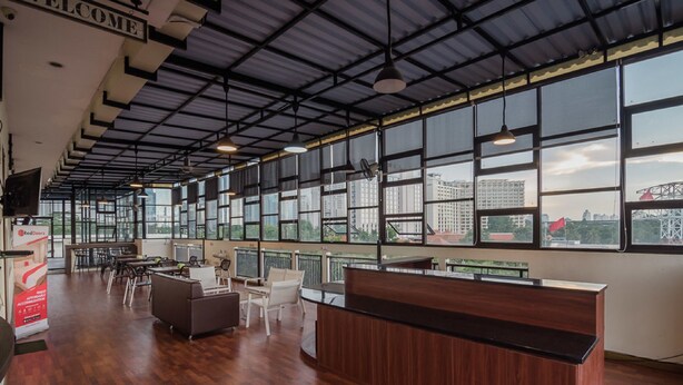 Amplia zona de recepción con un mostrador de madera, diversas opciones de asientos y grandes ventanales con vistas a la ciudad.