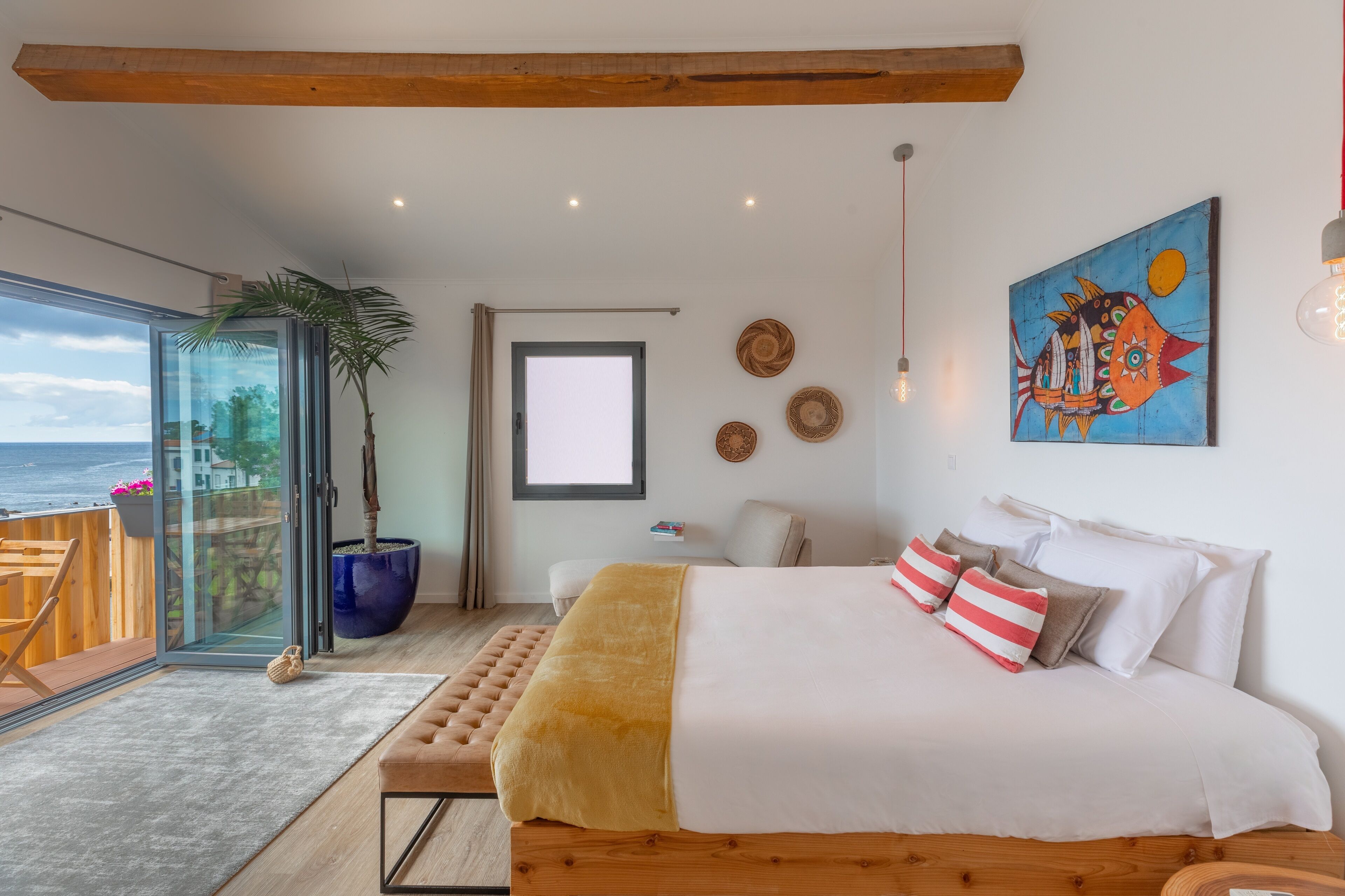 Un dormitorio con una cama grande, una planta en maceta, vista al mar y un balcón.