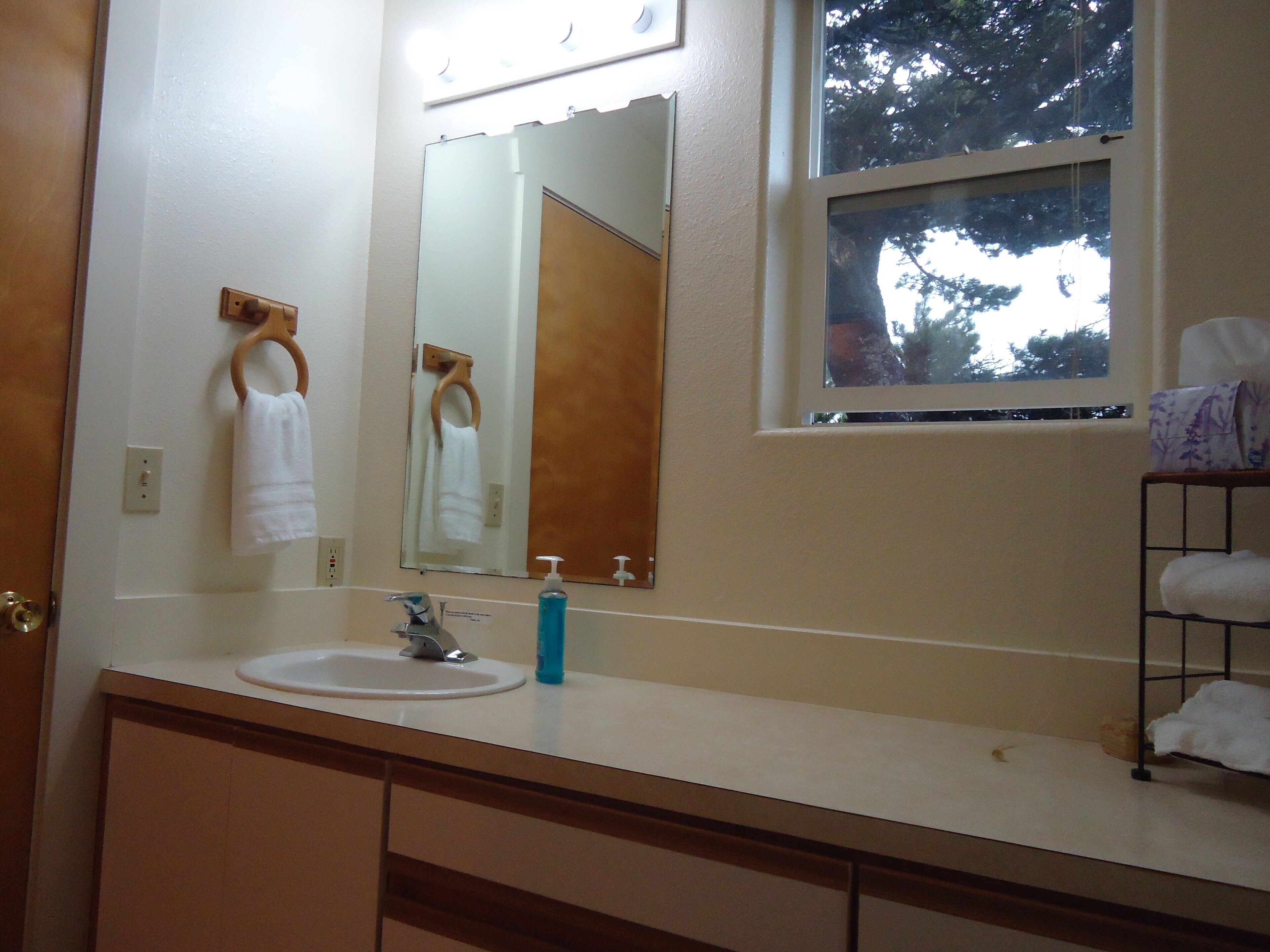 Un baño con lavamanos, espejo y ventana.