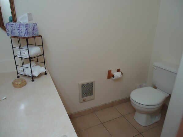 Un baño con un inodoro, un perchero con toallas dobladas, un dispensador de pañuelos y un objeto redondo pequeño en el suelo.