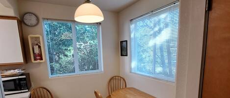 A compact kitchen with a dining table and chairs, a microwave, and a clock on the wall.