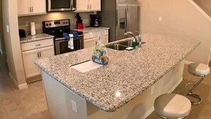 A kitchen with white cabinets, stainless steel appliances, a granite countertop, and a clock on the wall.