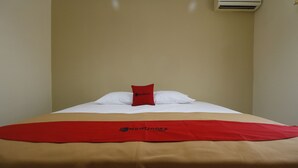 A hotel room with a bed covered in a beige and red blanket, a red pillow, and a white pillow. An air conditioning unit is mounted on the wall above the bed. - RedDoorz @ Jalan Gatot Subroto Jakarta (Jakarta)