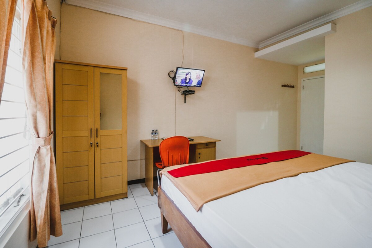 Ein Hotelzimmer mit einem Bett, einem Schreibtisch, einem Stuhl, einem Kleiderschrank und einem an der Wand befestigten Fernseher.