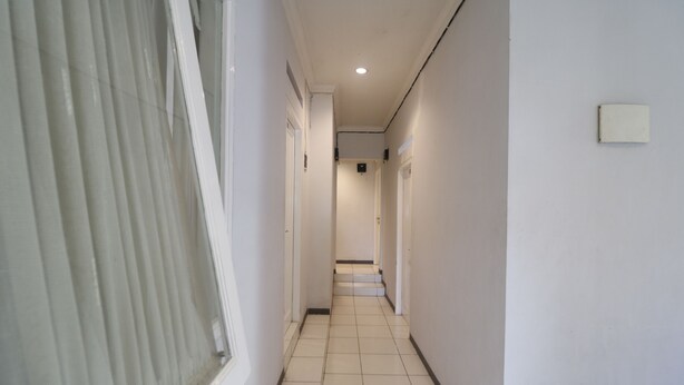 A narrow, tiled hallway with white walls and a window on the left. - RedDoorz @ Jalan Gatot Subroto Jakarta (Jakarta)