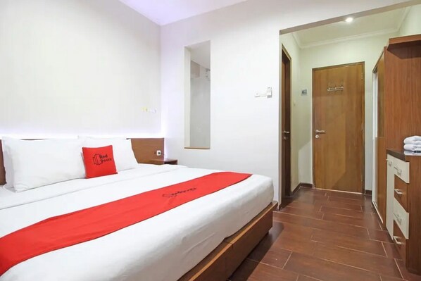A hotel room with a large bed, a red throw, and a wooden wardrobe.