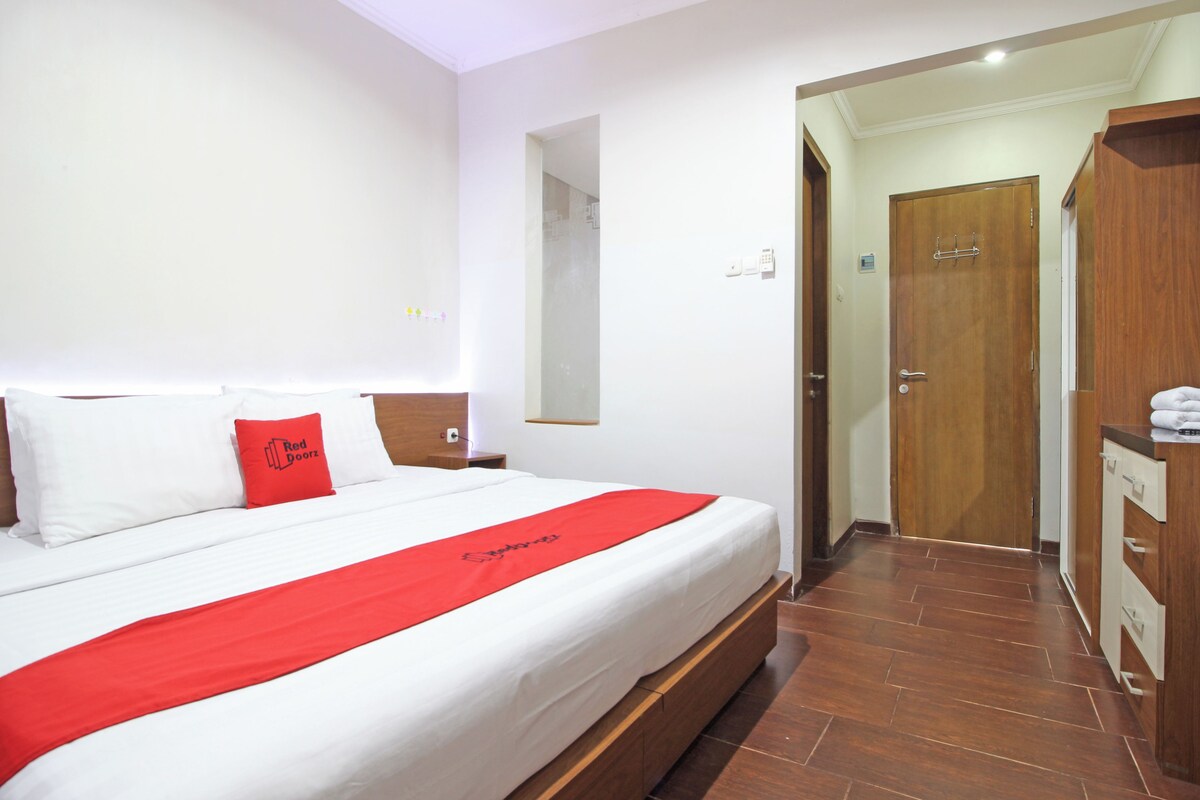 Habitación de hotel con una cama grande, un armario de madera, un baño con espejo y una puerta que da a otra habitación.