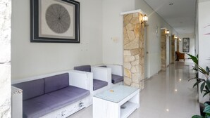 A hallway with a stone wall, a framed artwork, a white wicker sofa, and a small table. - RedDoorz near Jogja City Mall (Pogung Lor)