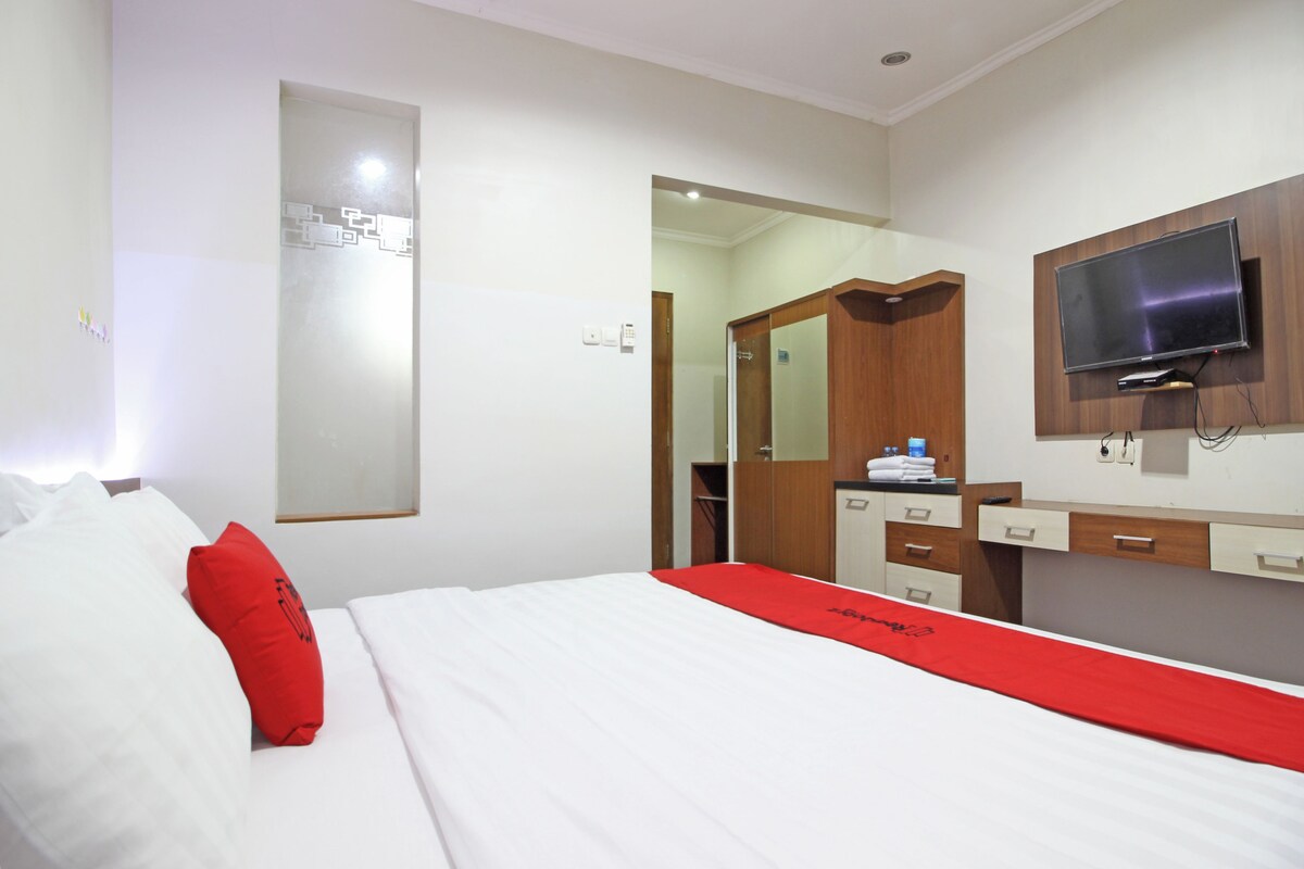 Ein Hotelzimmer mit einem Bett, einer roten Decke, einem an der Wand montierten Fernseher und einem Holzschrank.