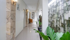 A corridor with stone walls, a wicker chair, and potted plants. - RedDoorz near Jogja City Mall (Pogung Lor)