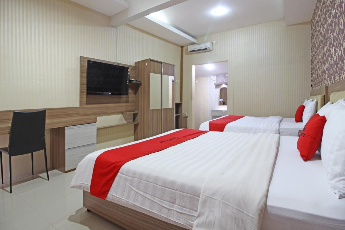 Habitación de hotel con dos camas, un escritorio, una silla y un televisor.