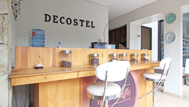 A bar area with a wooden counter, two white bar stools, and a wall with the word "DECOSTEL" above a logo. - RedDoorz near Jogja City Mall (Pogung Lor)