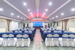 A conference room with rows of tables and chairs, a stage with a podium, and a large screen at the front. - Huangdu International Hotel (Jiange)