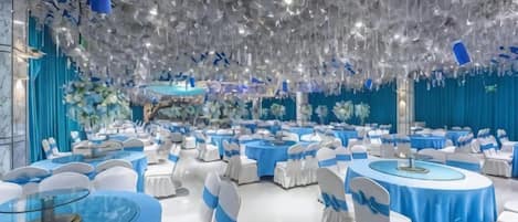 A banquet hall with round tables, white chairs, and a blue tablecloth theme.