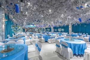 A banquet hall with round tables, white chairs, and a blue tablecloth theme.
