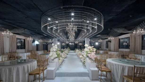 A banquet hall with round tables, chairs, and a central aisle decorated with flowers.