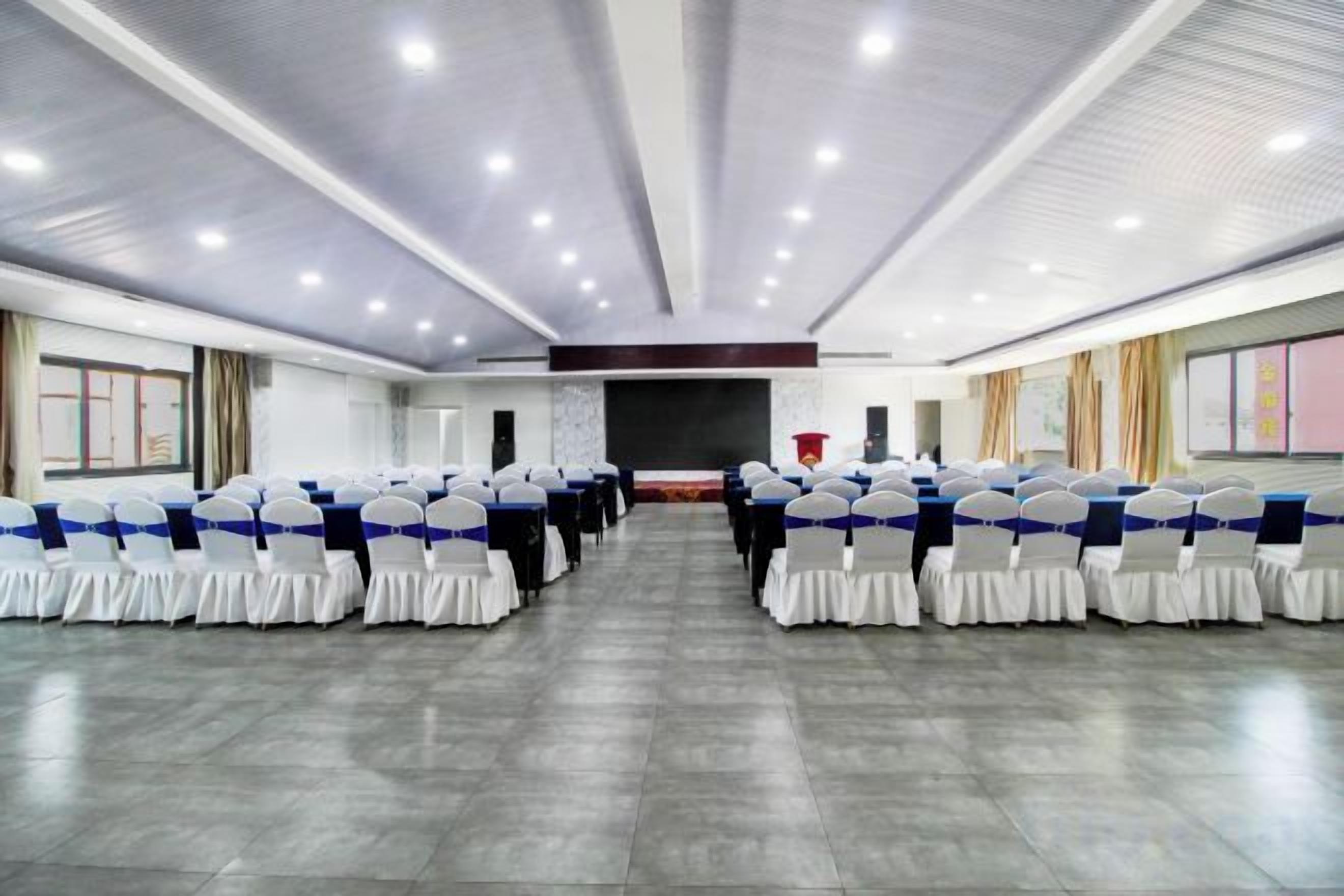 A conference room with rows of chairs, a stage, and a large screen.