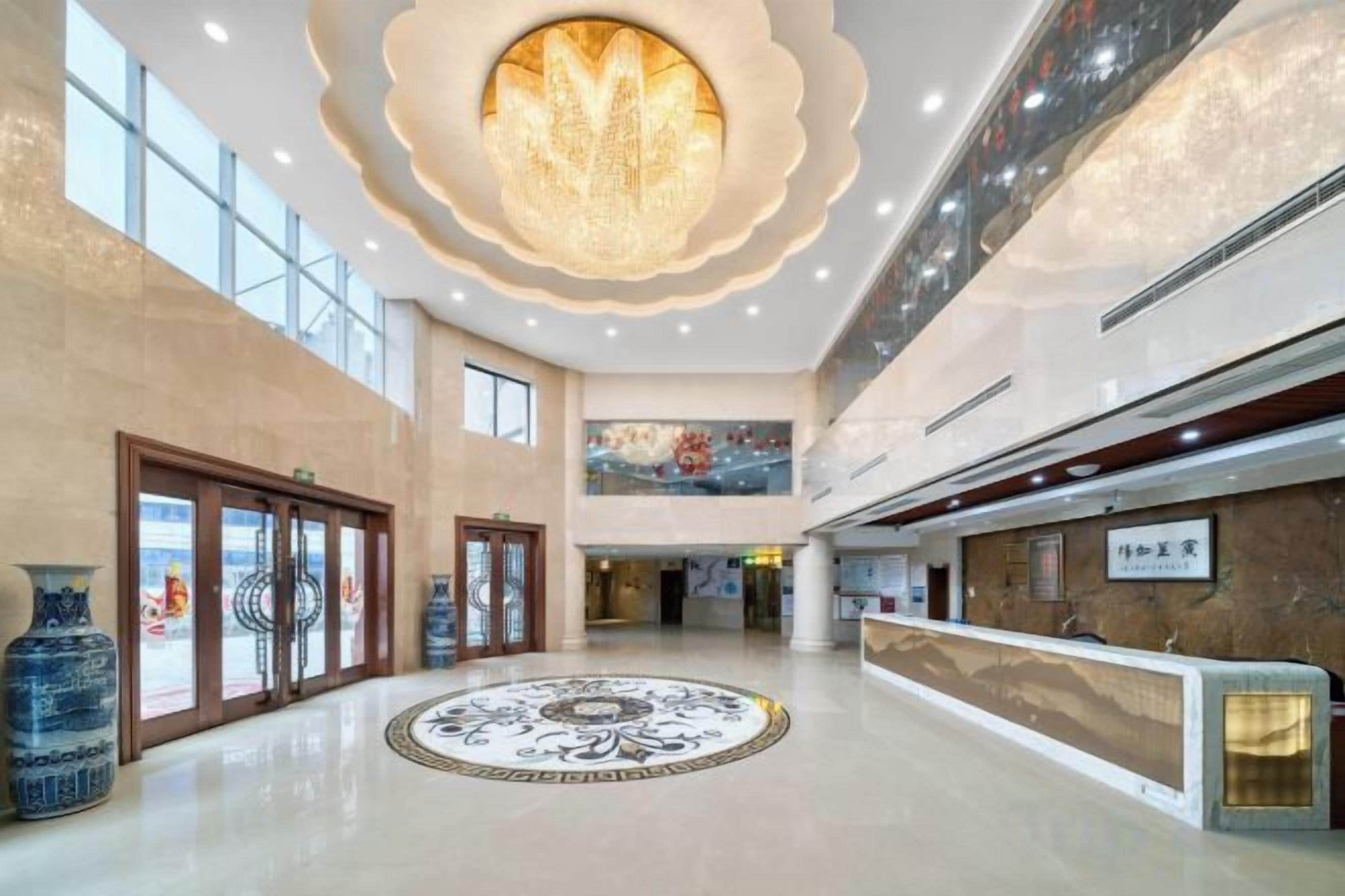 Un hall d’entrée spacieux avec un sol circulaire orné de motifs, un comptoir d’accueil et un grand lustre.