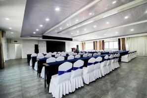 Une salle de conférence avec de longues tables et des chaises, une scène et une grande fenêtre.