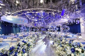 Un espacio con un pasillo central flanqueado por mesas y sillas, decorado con arreglos florales.