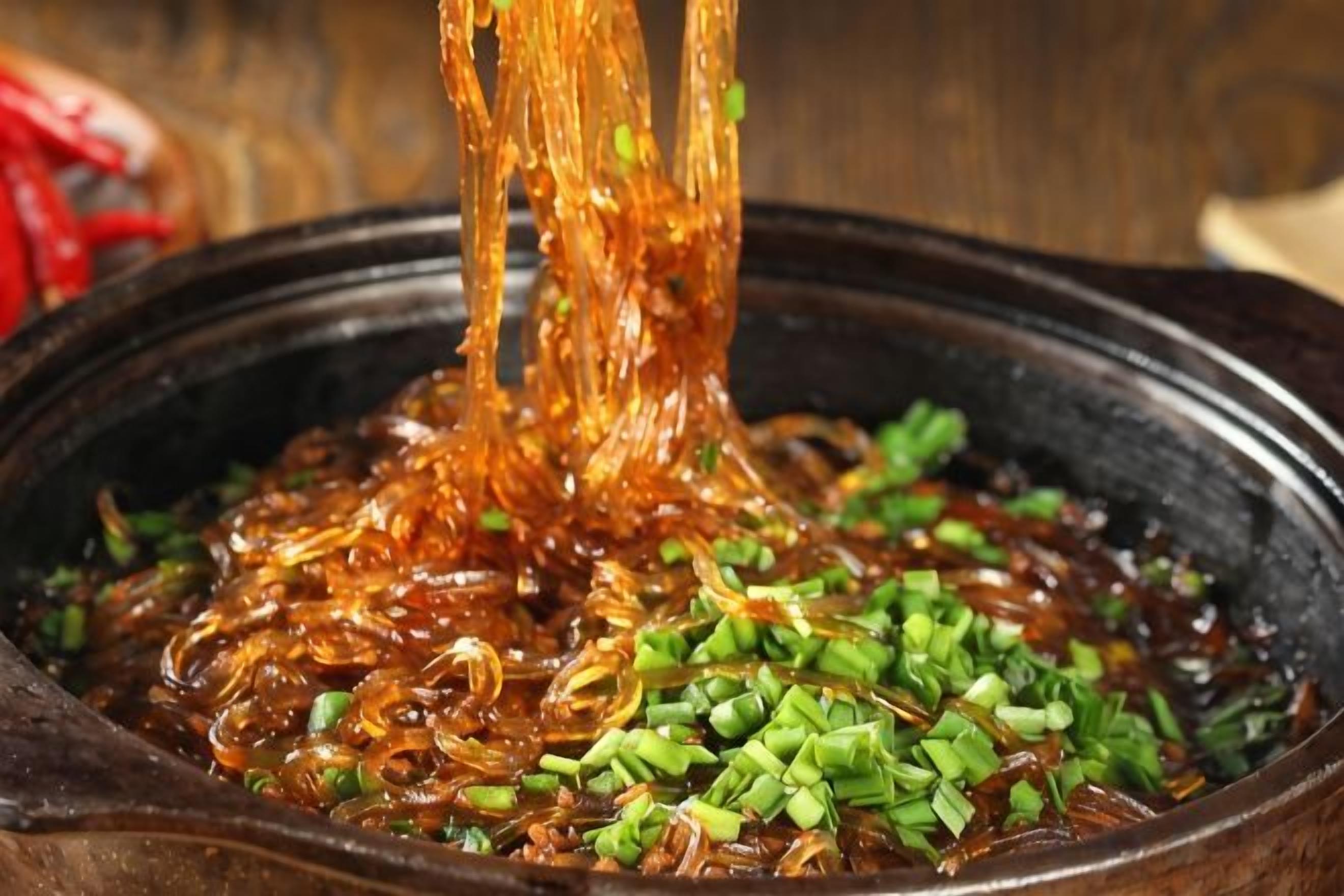 Un bol de nouilles est soulevé d’un liquide et garni d’oignons verts hachés.