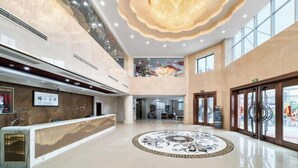 A spacious lobby with a reception desk, a decorative circular floor pattern, and a large chandelier.