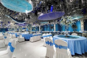 A banquet hall with round tables, white chairs, and blue tablecloths.