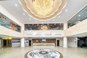 Un vestíbulo amplio con un mostrador de recepción central, una araña de cristal y un diseño decorativo en el suelo.