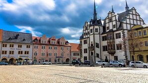 Ein Kopfsteinpflasterplatz mit historischen Gebäuden, darunter ein Hotel und eine Kirche mit einem Kirchturm.