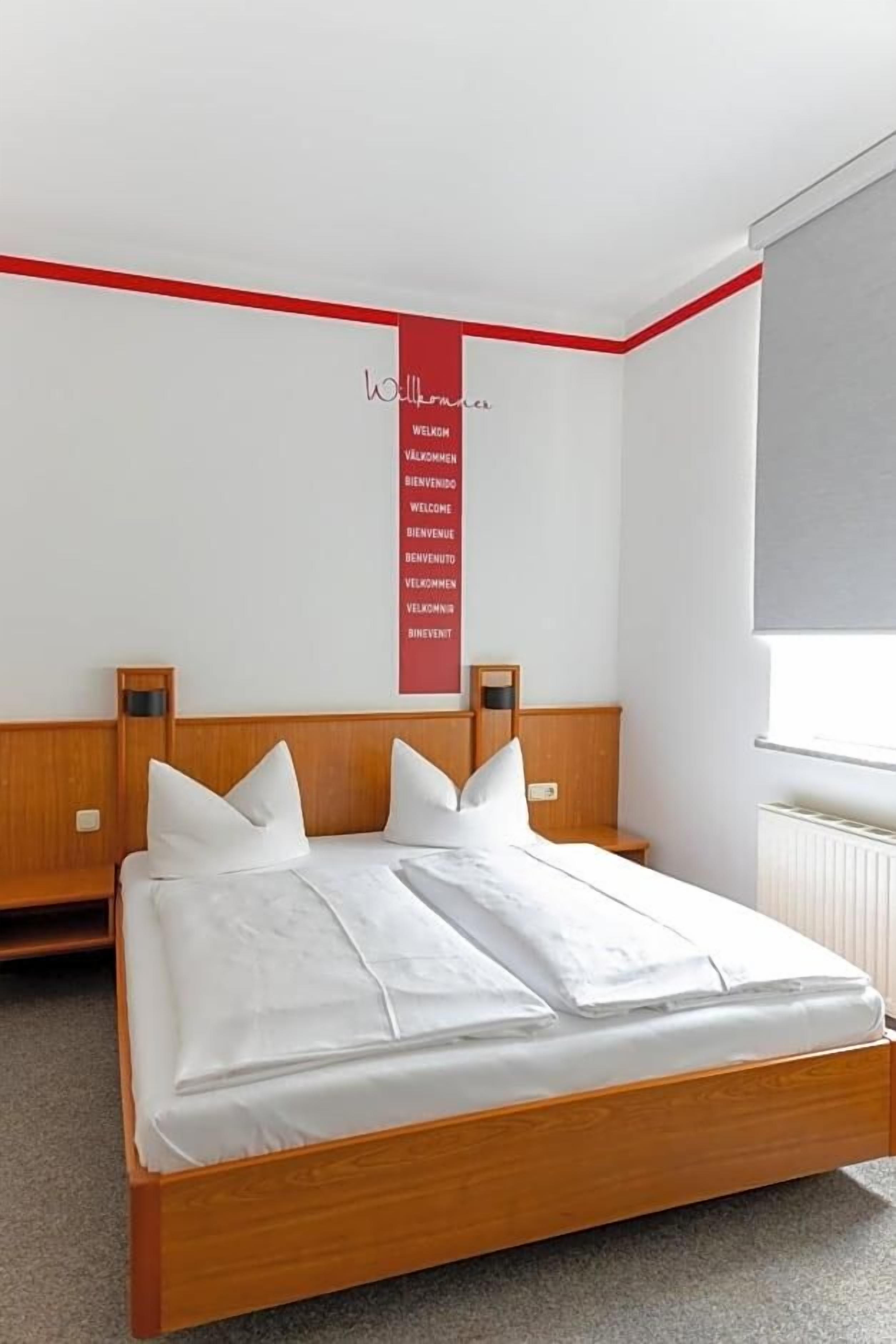Ein Hotelzimmer mit einem hölzernen Bett, weißer Bettwäsche, einer roten Akzentwand und einem Fenster.