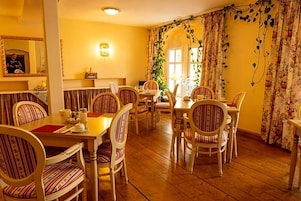 Comedor con mesas de madera y sillas a rayas, un espejo y una lámpara fijada a la pared.