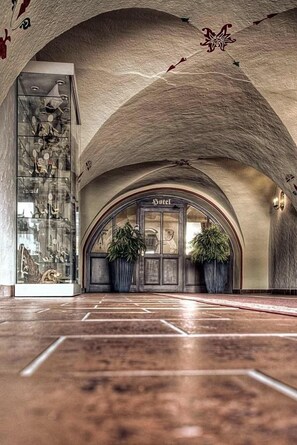 A hotel entrance with an arched ceiling, a glass display case with items, and two large potted plants. - Anker (Saalfeld-Saale)