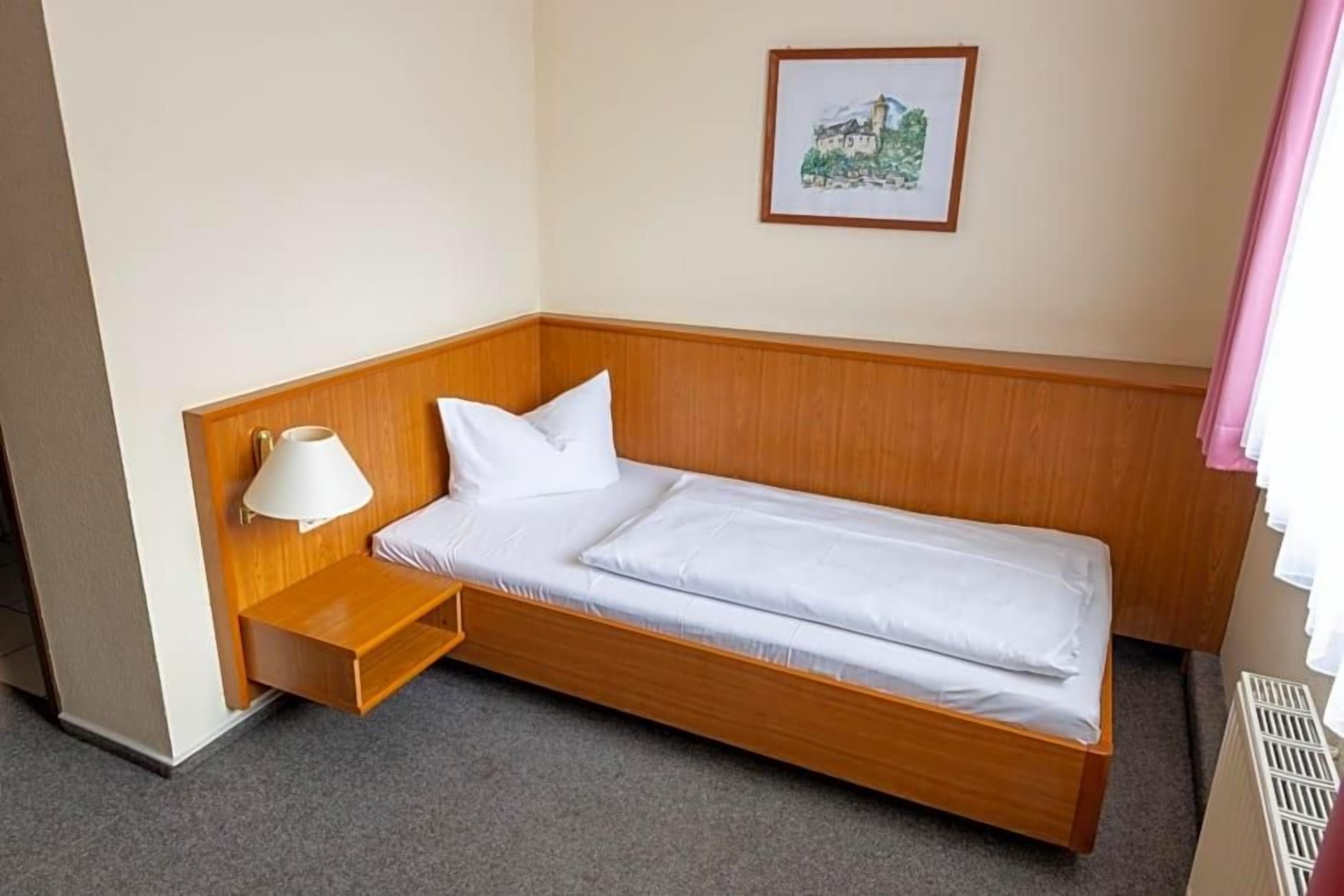 A single bed with a wooden headboard, a bedside table with a lamp, and a framed picture on the wall.