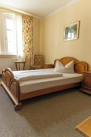 A bedroom with a wooden bed, a nightstand, a chair, a small table, and a painting on the wall.