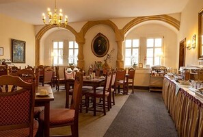 A dining area with wooden tables and chairs, a chandelier, and a portrait on the wall. - Anker (Saalfeld-Saale)
