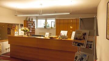 Ein Empfangstresen mit Holzbeschlag, ein Fenster mit Ausblick und ein Bücherregal mit Büchern und Dekoration.