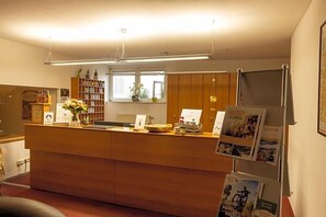 A reception desk with a wooden counter, a window with a view, and a bookshelf with books and decorative items.