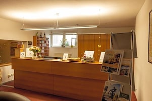 Balcão de recepção com bancada de madeira, janela com vista e estante com livros e objetos decorativos.