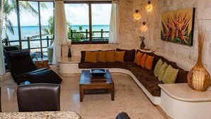A spacious living room with a curved sofa, a coffee table, and a view of the ocean through large windows. - Ocean view Condo, Large Private balcony over beach with jacuzzi, 2 pools, W/D (Playa del Carmen)