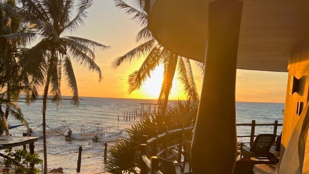 A pool area with a view of the sunset over the ocean, palm trees, and a deck with chairs. - Ocean view Condo, Large Private balcony over beach with jacuzzi, 2 pools, W/D (Playa del Carmen)