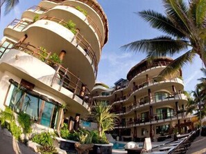 Un hôtel à plusieurs étages doté de balcons, d’une piscine et d’un aménagement paysager de style tropical.